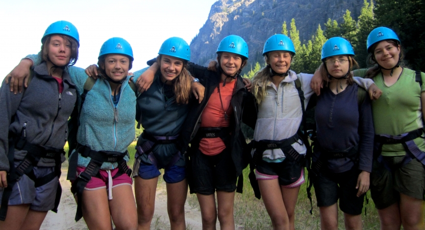 a group of outward bound students wearing blue helmets pose for a photo on a rock climbing course